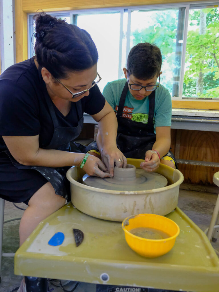 A camper and an instructor working on pottery.