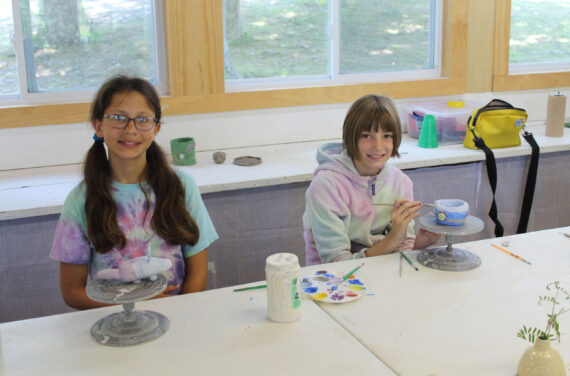 Two campers painting their pottery work.